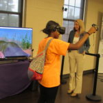 A cadet wearing virtual reality gear pets a manatee visible on a screen.